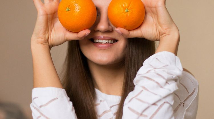 girl holding oranges to face